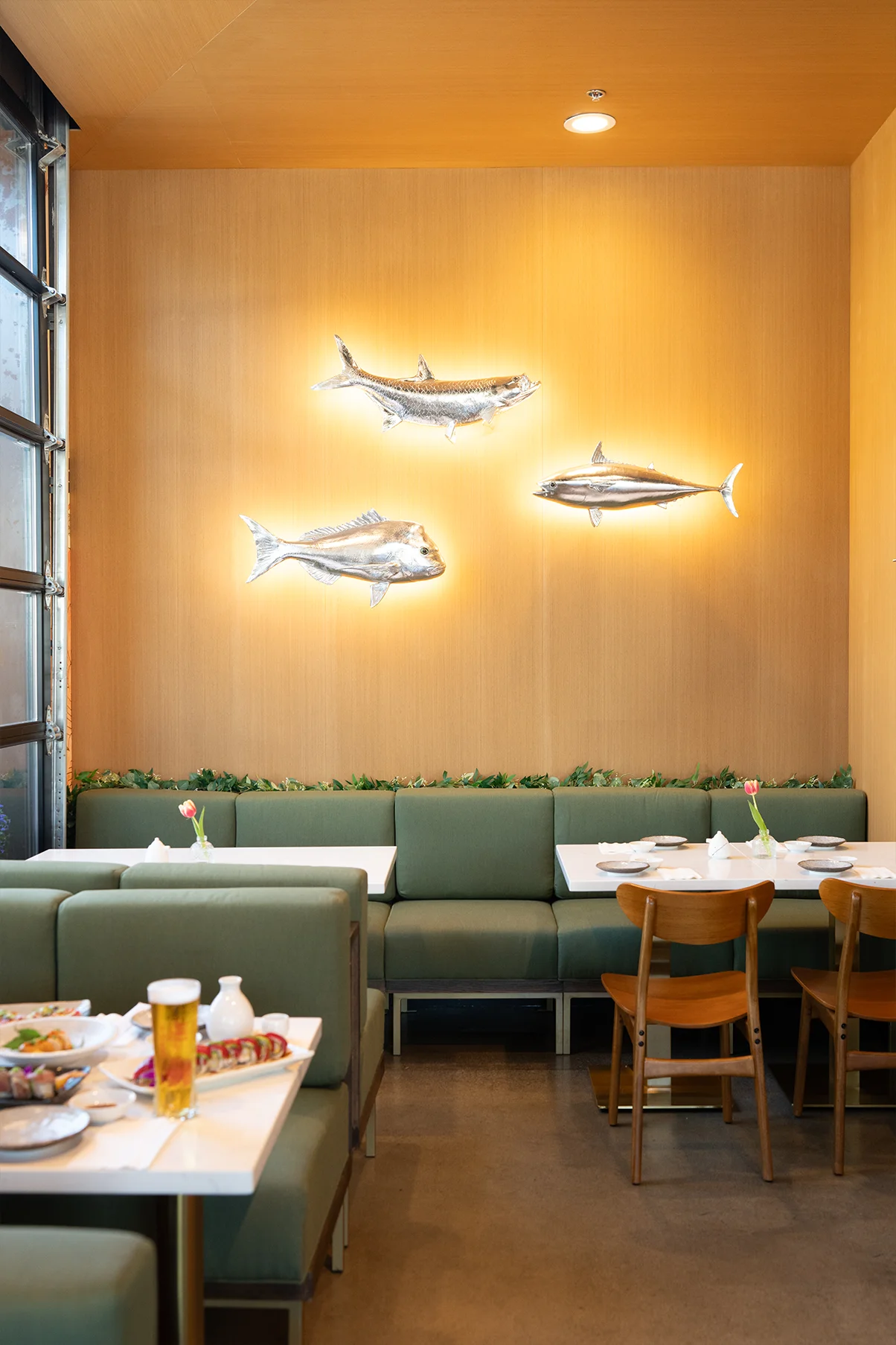 Sage booth seating beneath three silver fish sculptures on the wall at Fish Boon.